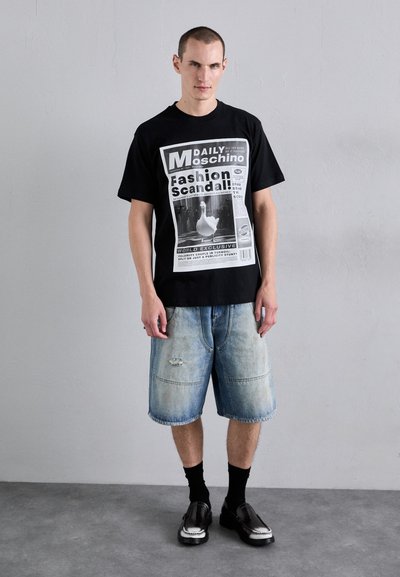 Tricou negru cu un print grafic ce seamănă cu o pagină de ziar, pantaloni scurți din denim albastru cu margini desfăcute și pantofi negri cu accente albe.
