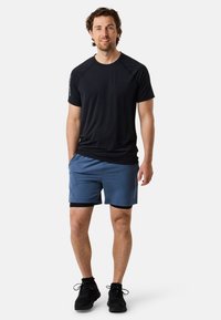 Svart kortärmad träningsskjorta i kombination med blå shorts. Outfiten har en enkel design med en vanlig passform och mörka skor.
