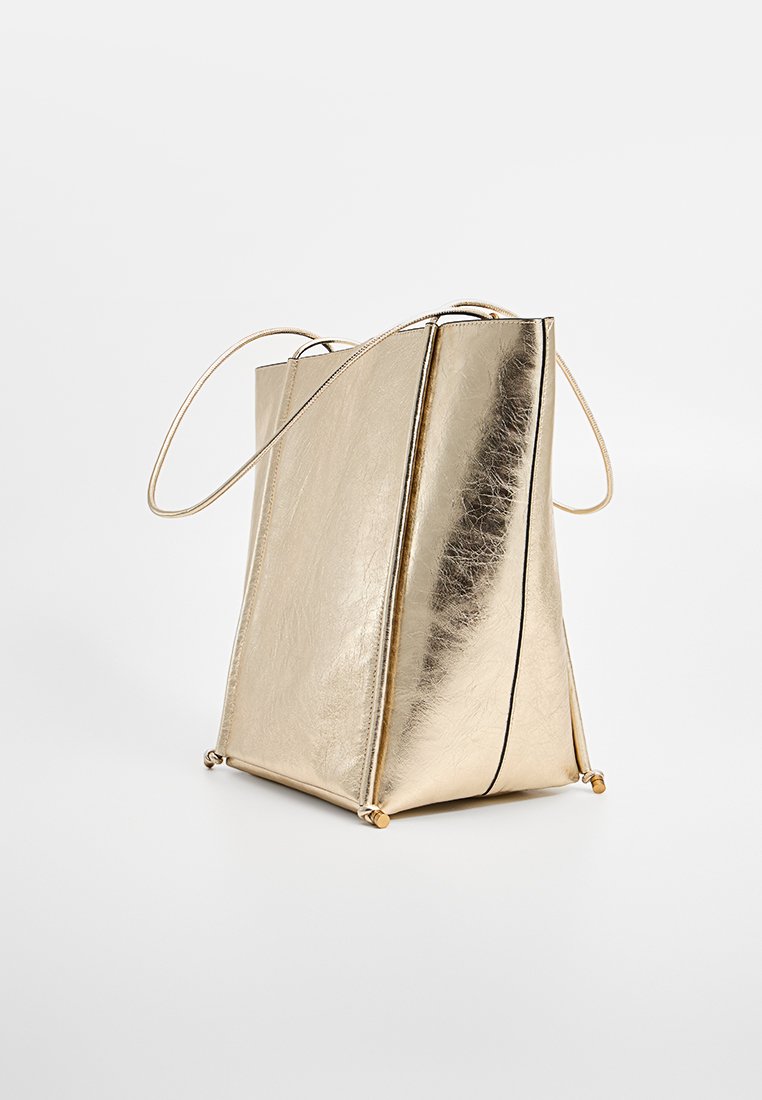 Goldfarbene metallische Handtasche mit strukturierter Form, dünnen Schulterträgern, Kontrastnähten und einer glänzenden, strukturierten Oberfläche.