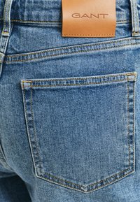 Blauwe denim jeans met een leren GANT-label op de tailleband. Voorzien van een standaard ontwerp voor achterzakken en contrasterende gele stiksels.