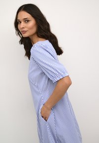 Kék és fehér csíkos ruha rövid puffos ujjakkal, oldalsó zsebekkel és laza szabással. Simább anyag, térdig érő fazon és kerek nyakú kialakítás.