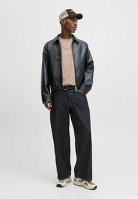 Zwarte faux leren jas met rits, beige t-shirt, donkerdenim wijde broek en crèmekleurige sneakers. Basketbalpet met een net achterzijde.