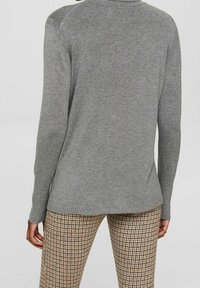 Grijze lange mouw gebreide trui met een ronde hals en geribbelde manchetten, gecombineerd met beige en bruine broek met een ruitpatroon.