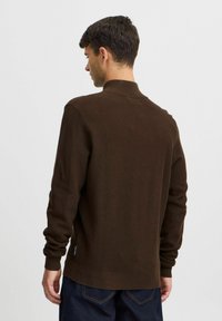 Brown textured pullover with a high collar, ribbed cuffs, and hem. Notable fabric pattern is woven, creating a subtle dimensional effect.