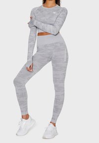 Graues Camouflage-Sportset mit einem langärmeligen Cropped-Top und hoch geschnittenen Leggings, die eine enganliegende Passform, elastisches Material und ein Logodesign aufweisen.