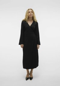 Zwarte wikkeljurk met lange mouwen, gestructureerde stof en een V-hals. De jurk heeft een aansluitende taille en loopt tot halverwege de kuit.