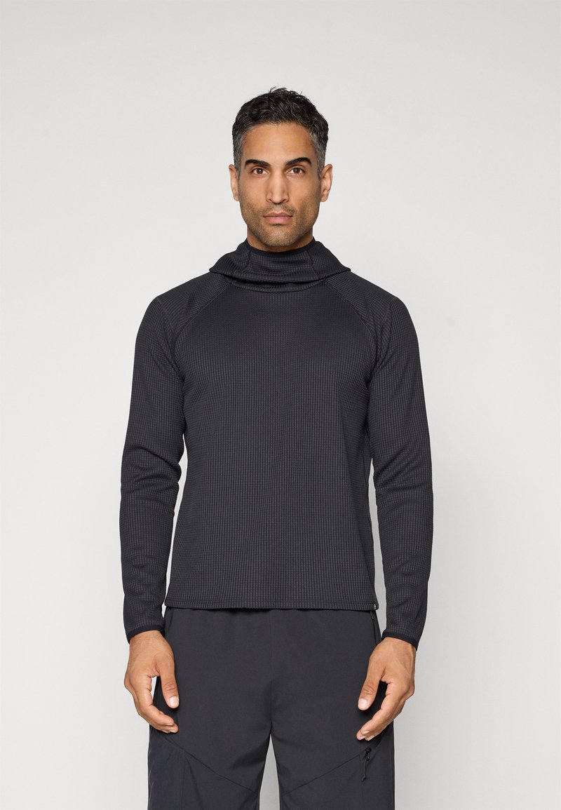 Svart termisk langermet topp med funnel neck, med en teksturert ribbestruktur og kontraststing, båret over mørke bukser.