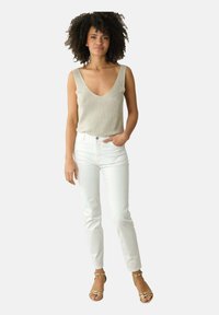 Haut sans manches beige clair avec un décolleté en V profond, associé à un jean blanc taille haute ; le modèle porte des sandales dorées à lanières.