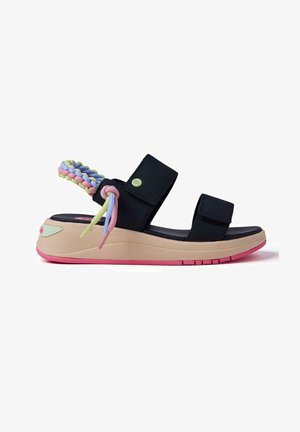 Sandalias de tela negra con suela gruesa beige, detalles en rosa y una correa trenzada multicolor. Cuentan con correas ajustables para un mejor ajuste.