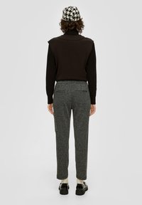 Zwarte trui met schouderdetails, grijze textuur broek met zakken, en een houndstooth hoed. Zwarte schoenen met een dikke zool.