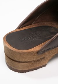 Bruna träsandaletter med en slät läderöverdel. Sulan har en formad design, präglad logotyp och en anmärkningsvärd trästruktur.