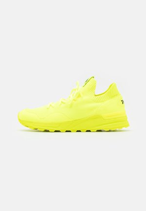 Zapatilla deportiva de color amarillo brillante con parte superior de punto, cierre de cordones y suela gruesa de goma, mostrada de lado sobre un fondo blanco.