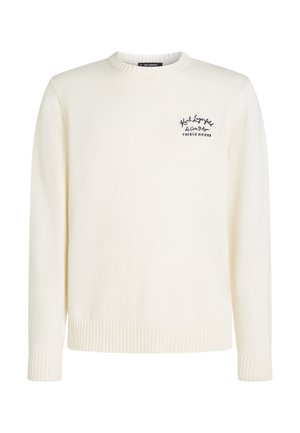 Maglione crema lavorato a maglia con scollo rotondo, polsini e orlo a coste, e un piccolo logo nero sul lato sinistro che raffigura la "Riviera Francese".