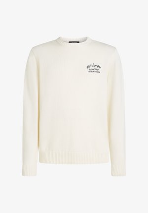 Kötött krémszínű pulóver kerek nyakkivágással, bordás mandzsettákkal és szegéllyel, valamint a bal oldalon egy kis fekete logóval, amely a "French Riviera" feliratot ábrázolja.