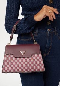 Maroon handbag with a geometric pattern. Made of synthetic material with a glossy finish. Features a triangular logo and detachable strap.