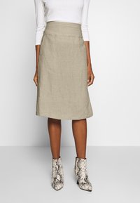 Beige linne A-linje kjol med hög midja och slät textur, i kombination med spetsiga ankelnboots i ett svart-vit ormtryck.