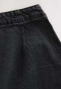 Black denim fabric with a slightly textured surface, featuring a stitched waistband and a simple, clean design.