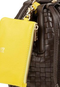 Bruine geweven leren tas met een felgele ritsvak eraan bevestigd. Bevat gouden hardware en een gladde textuur op beide materialen.