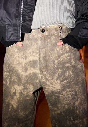 Bagi, jeans tie-dye dalam nuansa beige dan abu-abu yang lembut. Memiliki pinggang tinggi, desain lima saku, dan kain bertekstur dengan jahitan yang terlihat.