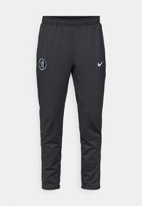 Svarte treningbukser laget av myk stoff, med elastisk midjebånd, sidelommer og en hvit Nike-logo på venstre ben.