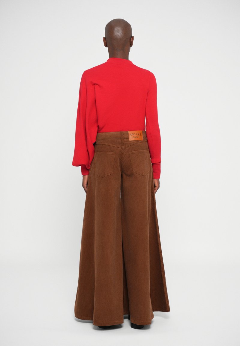 Red fitted long-sleeve top paired with wide-leg brown corduroy trousers featuring back pockets and a label at the waistband.