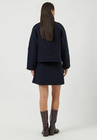 Mörkblå kort jacka och matchande kjol, texturerad tyg, lagerdesign, kombinerat med knähöga bruna läderstövlar.
