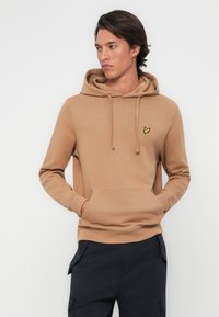 Felpa marrone in cotone con tasca frontale, cappuccio regolabile con cordini e piccolo logo ricamato giallo sul lato sinistro del petto. Tessuto morbido.