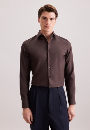 Camicia marrone a maniche lunghe con colletto classico, chiusura frontale con bottoni e bottoni grigio scuro, indossata con pantaloni blu navy. Texture liscia e uniforme.