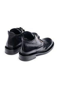 Black leather ankle boots with a smooth texture, rounded toe, and a low stacked heel. Features gold-tone eyelets and black laces.