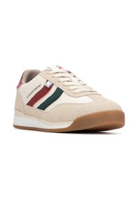 Zapatilla beige con materiales de gamuza y sintéticos. Presenta franjas verdes y rojas, una suela blanca y detalles de cordones en tonos neutros.