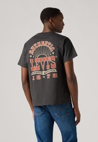 Crna pamučna majica s kratkim rukavima koja sadrži veliki retro stil crveni grafički dizajn na leđima s natpisima "AUTENTIČNI LEVI'S" i "1873", te opušteni kroj.