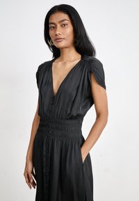 Robe noire avec un décolleté en V profond, manches courtes avec détail froncé, fermeture à boutons sur le devant et taille élastiquée.