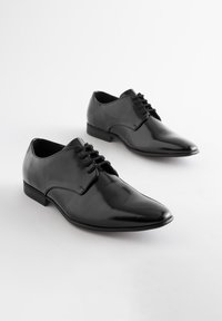 Black leather shoes with a glossy finish, featuring a pointed toe and textured sides, laced with thin black laces and a low heel.