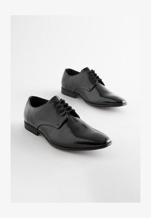 Scarpe in pelle nera con finitura lucida, caratterizzate da una punta affusolata e lati testurizzati, allacciate con sottili lacci neri e con un tacco basso.