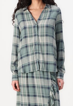 Koszula w zielono-granatową kratę, z długimi rękawami, zapinana na guziki, wykonana z miękkiego materiału, o luźnym kroju, z zaokrąglonym dołem, zestawiona z pasującą spódnicą.