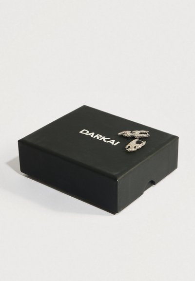 Črni pravokotni škatla z napisom "DARKAI" in na vrhu prikazane tri srebrne s s kristali okrašene sponke za lase.