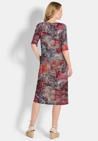 Frau, die ein knielanges Kleid mit Ellbogenärmeln trägt, das mit einem bunten Blumen- und abstrakten Muster verziert ist, kombiniert mit beigen Keilsandalen.