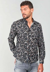 Camisa negra de botones con un patrón floral en blanco y naranja, de manga larga y corte entallado. Fabricada con un tejido ligero.