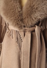 Καφέ μάλλινο παλτό με γιακά από συνθετική γούνα, με φραγμένα διακοσμητικά στοιχεία και ζώνη που δένει. Μαλακή υφή και κομψός σχεδιασμός.
