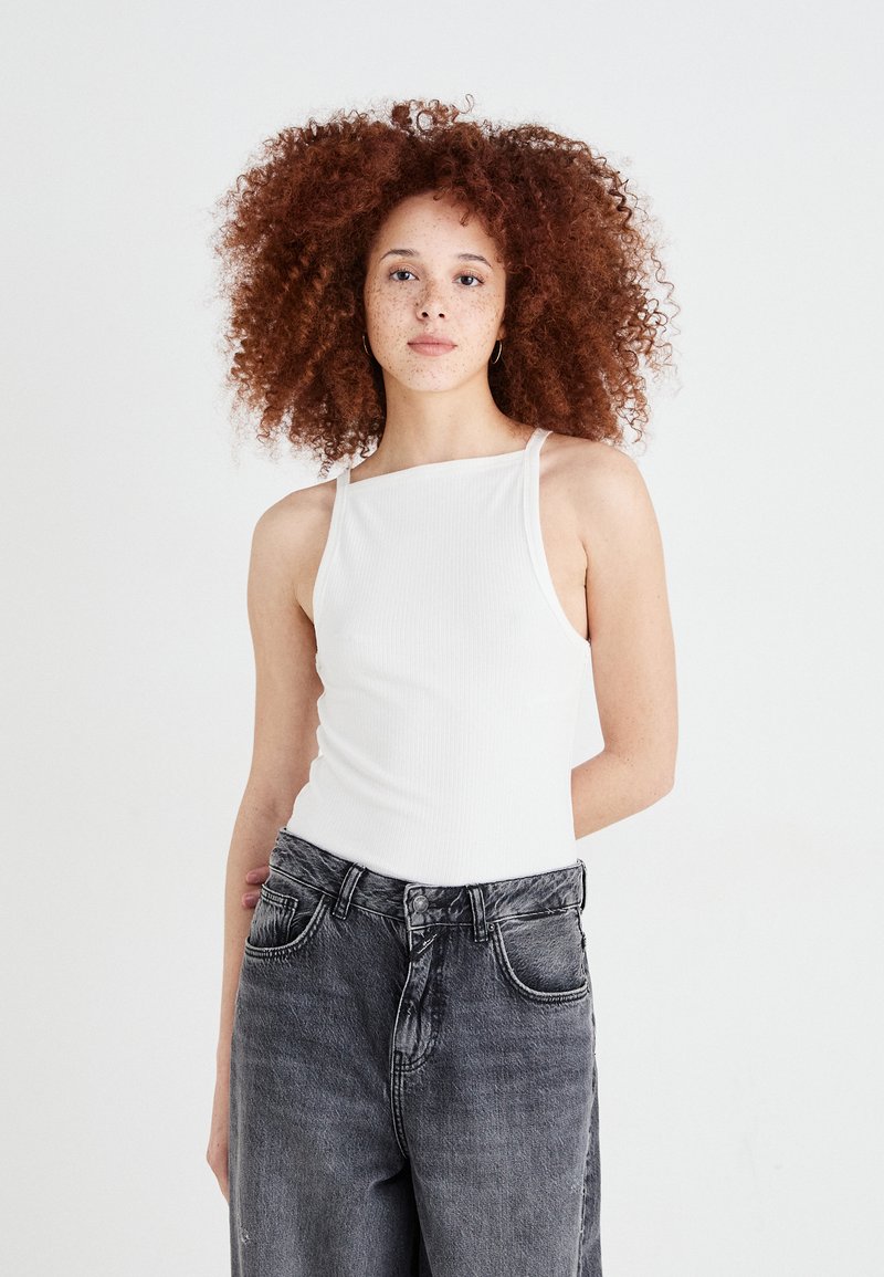 Hvit ribbet tanktop med tynne skulderstropper, kombinert med høytlivet, falmede svarte jeans med en løs passform og synlige sømmer.