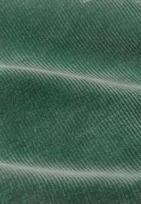 Grüner Cordstoff mit erhöhten Rillen, weichem Griff und glatter Oberfläche, durchgehend einheitlicher Farbe und strukturiertem Muster.