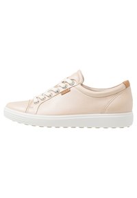 Beige leather sneaker with white rubber sole, round toe, metal eyelets, and a tan accent on the heel. Smooth texture and minimalist design.