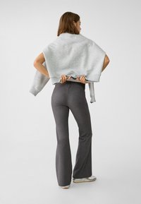 Un sweatshirt gris drapé sur les épaules, associé à un pantalon évasé foncé et ajusté. La texture est lisse, avec des lignes simples et sans motifs.