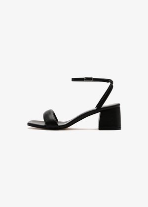 Sandales à talons noires avec une tige en cuir lisse, présentant une large sangle sur l'orteil et une sangle fine à la cheville. Le talon épais offre de la stabilité.