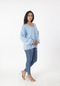 Maglione lavorato a maglia blu chiaro con scollatura a V e maniche lunghe e voluminose, abbinato a jeans in denim attillati e sandali con tacco trasparente.