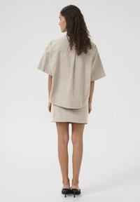 Beige fabric shirt with short sleeves, back seam detail, paired with a matching mini skirt. Smooth texture and simple design.