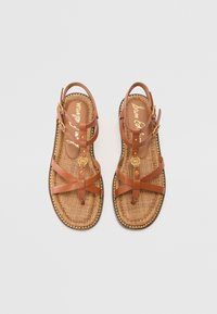 Brune lær sandaler med flere krydsede stropper, en vævet tekstur indersål og guldtone hardware accenter. Flad sål med en dekorativ kant.