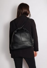Zaino in pelle nera dalla forma arrotondata, con spallacci doppi e tasche frontali con zip. Presenta una superficie texturizzata e accessori in metallo.