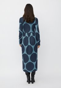 Abito a maniche lunghe con sfondo teal e grandi cerchi blu navy. Il materiale sembra morbido, con una vita aderente e una gonna fluente.