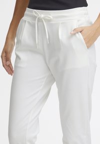 White jogger pants made of soft fabric feature a drawstring waist, side pockets, and a relaxed fit with subtle pleats.